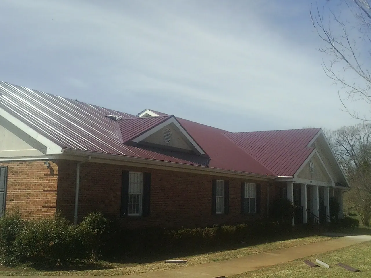 Red metal roof with gabled entries on a long brick building, from a Hail Damage Roof Repair job in Richlandtown