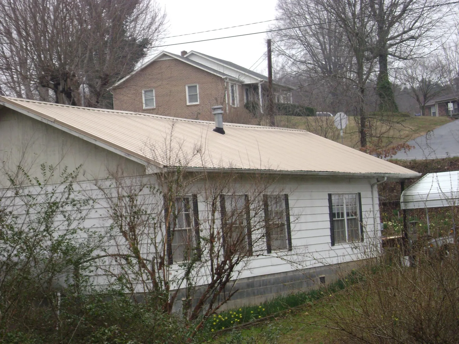 Tan metal roof on a white sided house set into a hillside — Commercial Roofing by Roofing Brothers in Richlandtown
